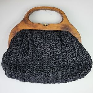 Woven black handbag with wooden handles and metal closure.
